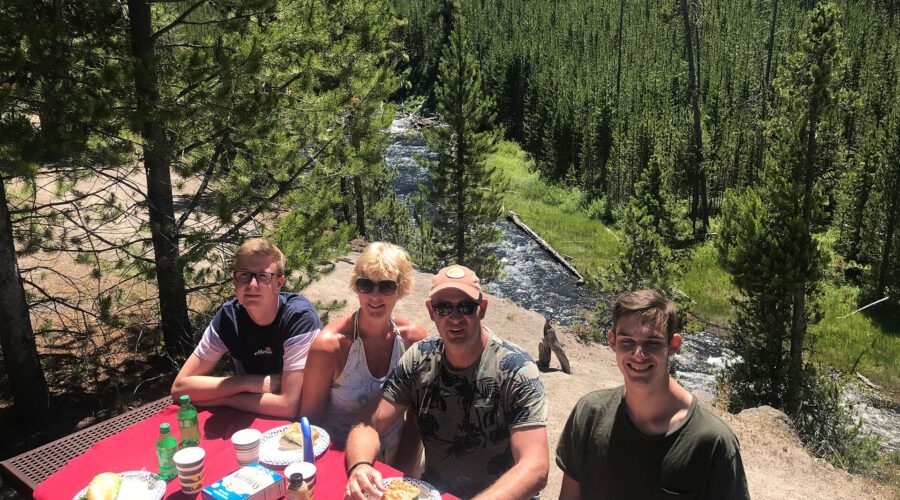A young family eats a picnic lunch next to a river in Yellowstone National Park. A couple watches as Old Faithful geyser erupts in Yellowstone National Park. Taken on a Teton Excursions tour of Yellowstone National Park.